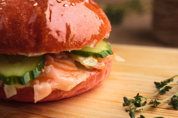 Concept: restaurant menus, healthy eating, homemade, gourmands, gluttony. Trendy glossy burger with salmon in pink bun with ingredients on messy vintage wooden background.