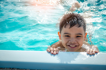 Portrait of asian kid laughing in a swimming pool. Sunlight filter process.