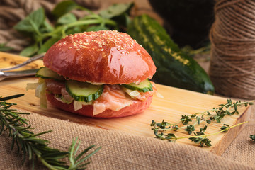 Concept: restaurant menus, healthy eating, homemade, gourmands, gluttony. Trendy glossy burger with salmon in pink bun with ingredients on messy vintage wooden background.