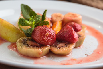 Concept: restaurant menus, healthy eating, homemade, gourmands, gluttony. White plate of fruit flambe. Apple, orange, strawberry, kiwi flambeed in cognac. On weathered wooden table.