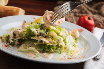 Concept: restaurant menus, healthy eating, homemade, gourmands, gluttony. White plate of salad with tiger prawns, flambeed in cognac, parmesan and cream with cutlery on vintage wooden table. Detail