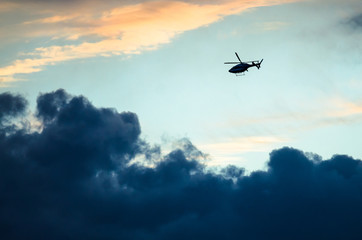 Obraz na płótnie Canvas Silhouetted Helicopter Flying Across a Sunset Sky