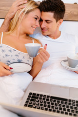Obraz na płótnie Canvas Couple relaxing in bed with coffee and laptop