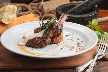 Concept: restaurant menus, healthy eating, homemade, gourmands, gluttony. White plate of lamb rack on wooden table and ingredients on background.