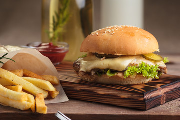 Concept: restaurant menus, healthy eating, homemade, gourmands, gluttony. Classic burger with beef with ingredients and french fries on messy vintage wooden background.
