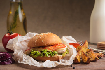 Concept: restaurant menus, healthy eating, homemade, gourmands, gluttony. Classic burger with chicken with ingredients and potato wedges on messy vintage wooden background.