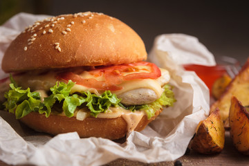 Concept: restaurant menus, healthy eating, homemade, gourmands, gluttony. Classic burger with chicken with ingredients and potato wedges on messy vintage wooden background.