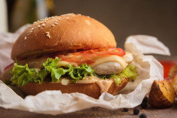 Concept: restaurant menus, healthy eating, homemade, gourmands, gluttony. Classic burger with chicken with ingredients and potato wedges on messy vintage wooden background.