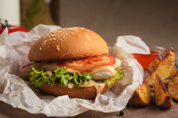 Concept: restaurant menus, healthy eating, homemade, gourmands, gluttony. Classic burger with chicken with ingredients and potato wedges on messy vintage wooden background.