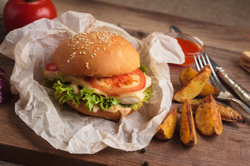 Concept: restaurant menus, healthy eating, homemade, gourmands, gluttony. Classic burger with chicken with ingredients and potato wedges on messy vintage wooden background.