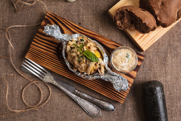 Concept: restaurant menus, healthy eating, homemade, gourmands, gluttony. Baked potatoes with mushroom sauce served in foil plate with ingredients and vintage cutlery on sackcloth background.