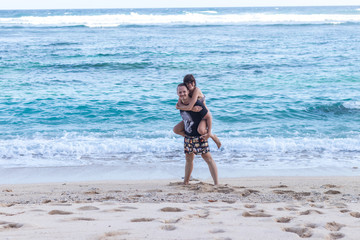 Young happy couple having fun on a tropical resort's white beach of Bali island, Indonesia.