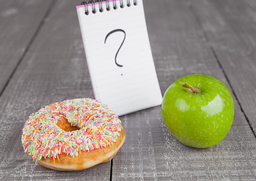Donut and apple healthy food choices on wooden board
