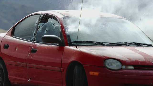 A tight shot of a red car shot up by bullets in slow motion.