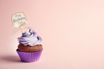 Delicious cupcake with greeting card on color background. Text HAPPY BIRTHDAY TO YOU on card.