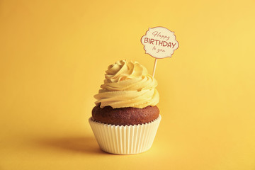 Delicious cupcake with greeting card on yellow background. Text HAPPY BIRTHDAY TO YOU on card.