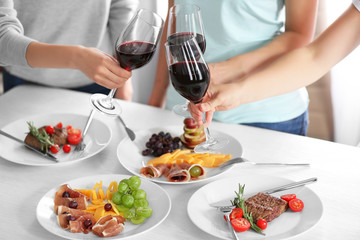 Women clinking glasses with wine and delicious dishes on table in restaurant