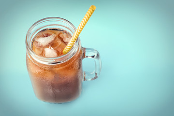 Jar of iced coffee with milk and straw on blue background