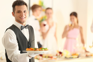Handsome young waiter with plate full of tasty tartlets at party