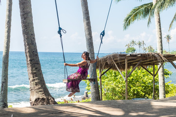 Sexy young woman sitting on the swing on the tropical beach, paradise island Bali, Indonesia. Sunny day, happy vacation in Asia.