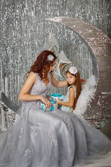 Mother and daughter are waiting for Christmas. Mom dressed fairy fairy gives her daughter gift. Happy parenting and childhood. Family holidays.