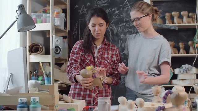 Happy young women standing in workshop and looking at finished papier-mache horse toy, then celebrating and hugging 