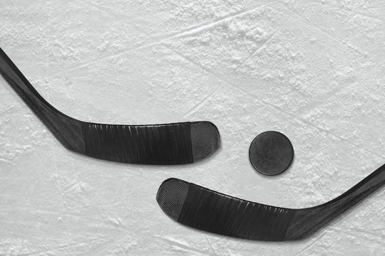 Hockey puck and a pair of black sticks on the ice
