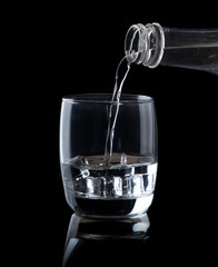 Pouring water drink in to glass with ice on a black background
