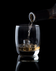 Pouring whiskey into glass  isolated on black background