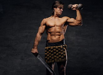 Fototapeta na wymiar Shirtless muscular male holds the sword and dumbbells.
