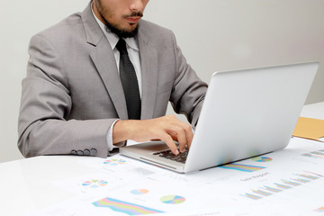 Young man working with laptop, man's hands on notebook computer, business person at workplace over business report papers,data,statistic