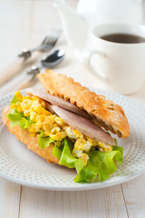 Sandwich stuffed with scrambled eggs, ham and lettuce leaves on a light wooden background. Selective focus.