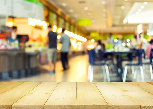 Defocused or blurred photo of food court montage with wood table top use for background.