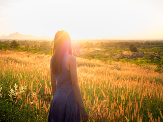 Fototapeta na wymiar Beautiful girl in stylish summer dress walking in the field with flowers in sunlight,enjoying freedom feeling happy at sunset