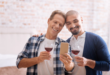 Delighted non-traditional couple drinking wine and taking selfie