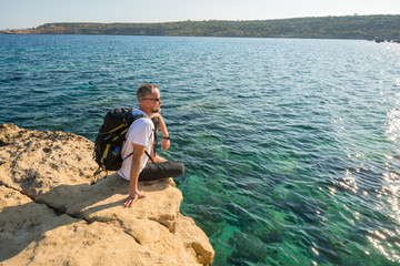Fototapeta na wymiar Bearded man with backpack sits and looking at sea