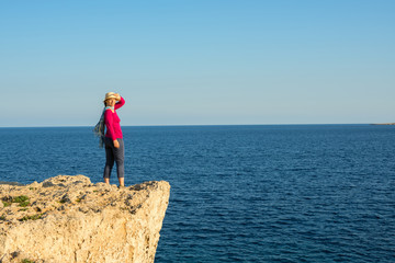 Woman in a straw hat standing on the rocky shore