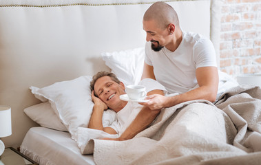 Cheerful homosexual couple having the breakfast in the bed