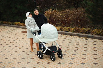 Family walk in the autumn park with a pram. Mom, dad and baby ou