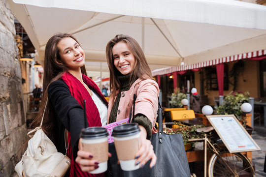 Two cheerful young women holding cups of coffee to go