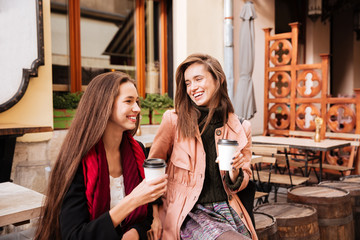 Two cheerful women with cups of coffee talking and laughing