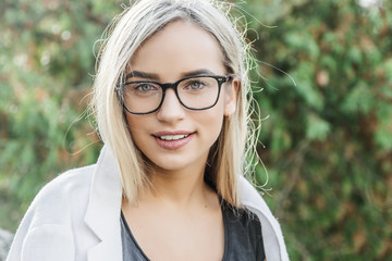 portrait of a young woman, blonde, glasses, outdoors in the park