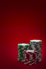 Casino and gambling concept with three stacks of chips of different colors ( red, green and white/ grey) isolated on a red felt with copy space
