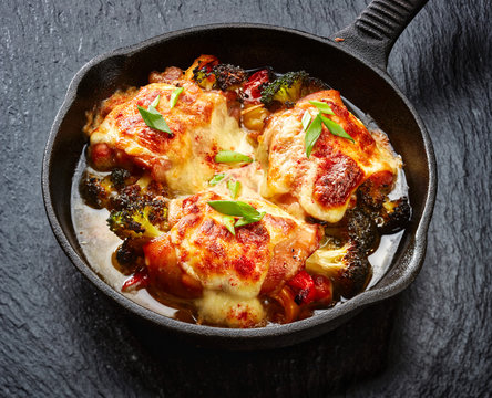 Roasted teriyaki chicken thighs  stuffed with vegetables, baked with mozzarella cheese on a black stone background