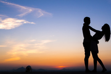 Obraz premium Silhouette of Happy Young Couple playing with cat Outside at Sunset