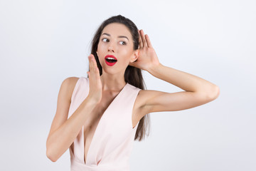 Woman holds her hand near ear and listens carefully on white bac