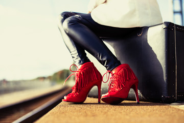 Fototapeta na wymiar Woman irn red high heels sitting on suitcase
