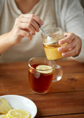 close up of woman adding honey to tea with lemon