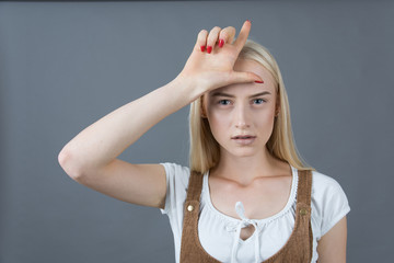 School blonde girl showing loser sign studio gray background