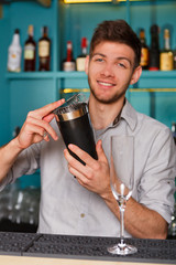 Young handsome barman in bar shaking and mixing alcohol cocktail